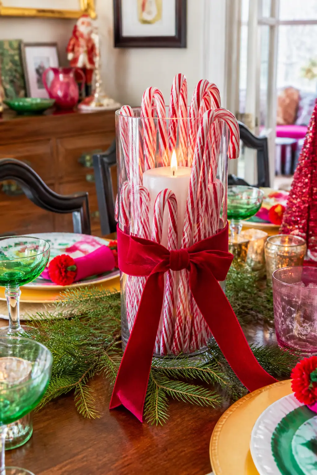 Candy Cane Centrepiece — A tall glass cylinder vase filled with candy canes standing upright, with a pillar candle set inside among them, is a centrepiece that