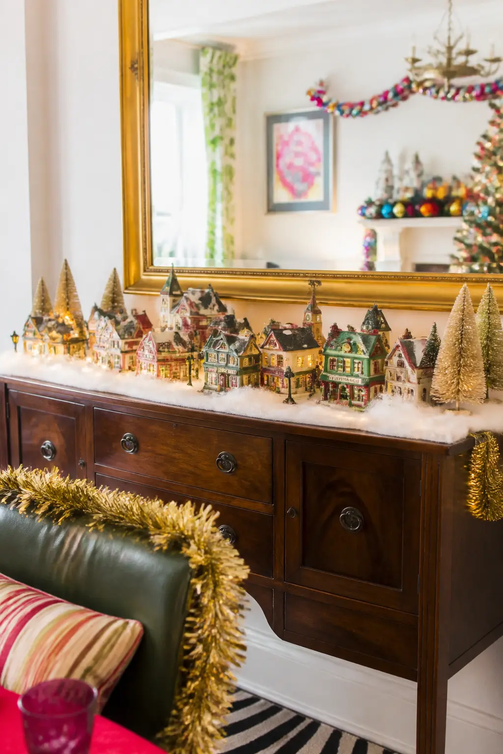 Village Scene Sideboard — A collection of ceramic or porcelain village houses, churches, and shops arranged on a sideboard with a layer of fake snow underneath