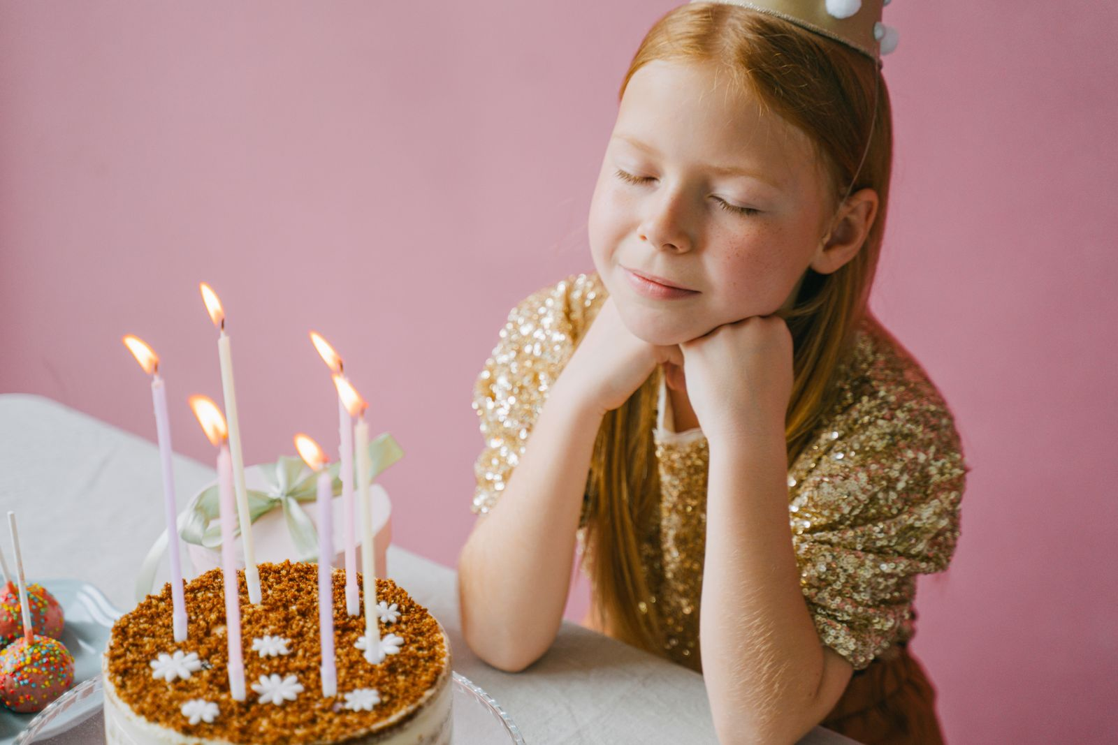 A young girl with a party hat enjoys her birthday with a cake and candles.