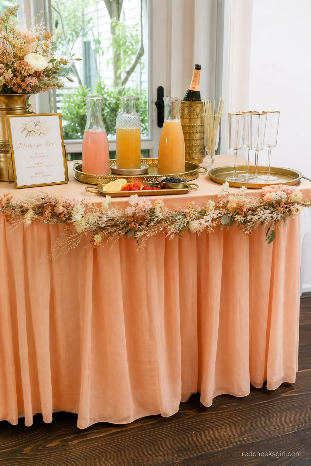 Apricot and Brass Mimosa Bar — A side table skirted in apricot linen and dressed with brass trays, juice carafes and a small sign, lets guests build their own