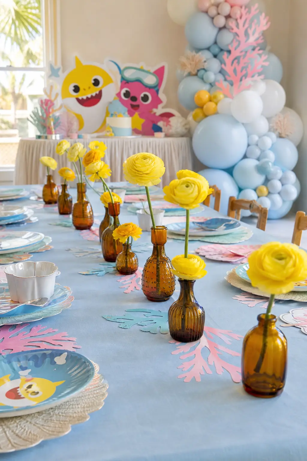 Amber Bud Vases Along the Table — A row of small amber glass bud vases, each holding a single yellow ranunculus stem, runs down the center of the guest table