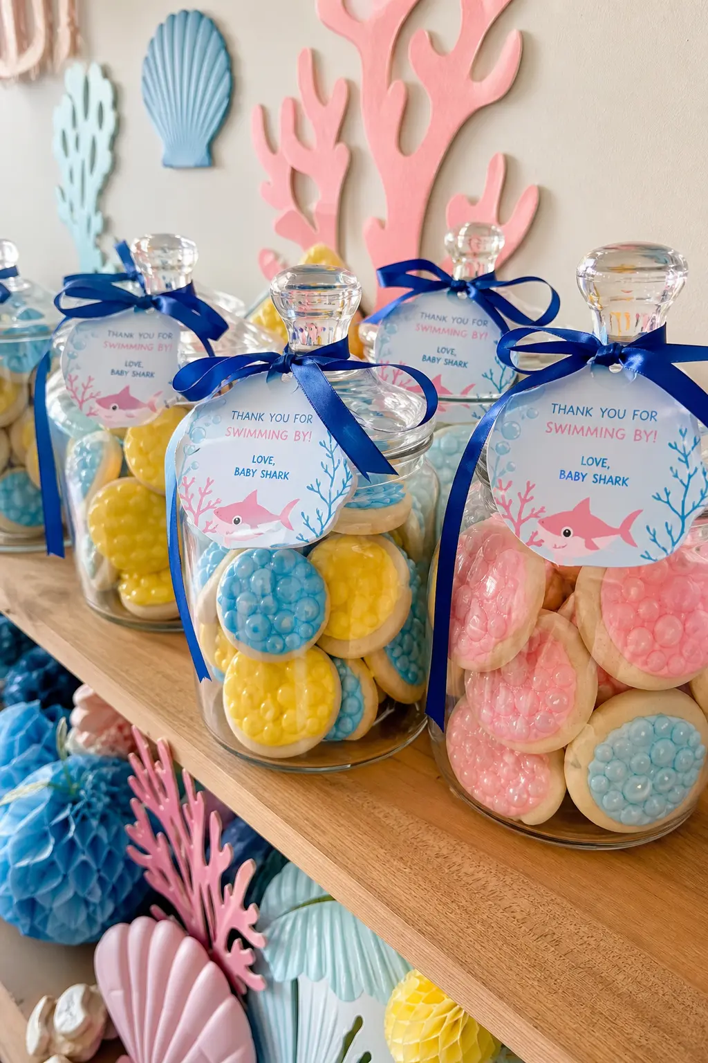 Bubble Cookie Favor Jars — Round sugar cookies iced to look like bubbles, stacked in clear glass jars tied with cobalt ribbon, sit on a shelf as both display