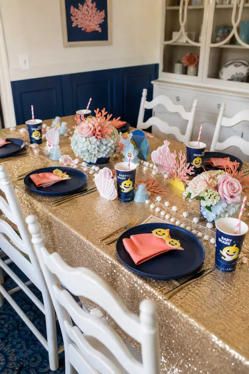 Sandy Gold Place Setting — A gold sequin tablecloth under navy plates and coral napkins gives the guest table a warm, sandy undertone instead of the usual cool