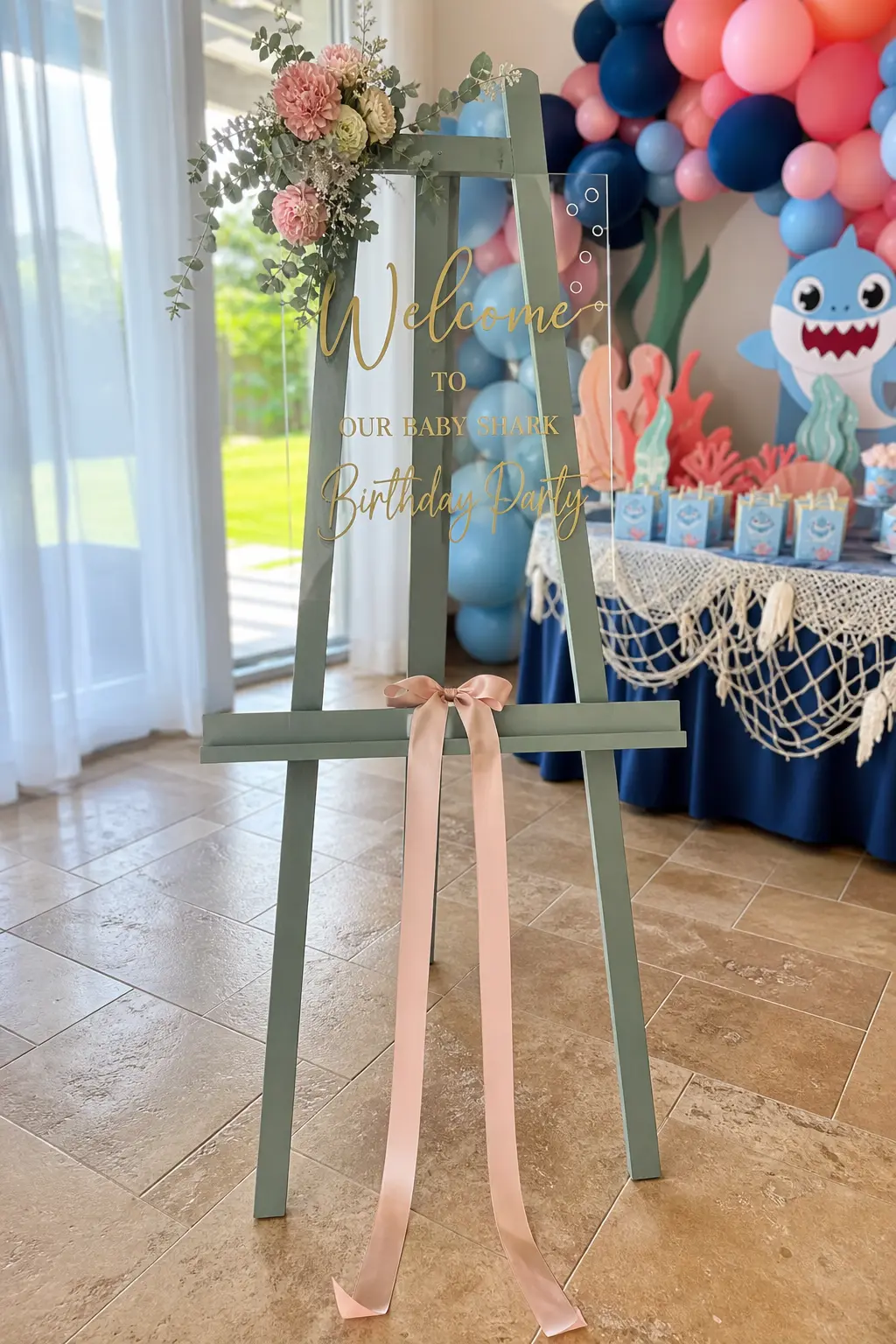 Wooden Welcome Sign Easel — A sage green painted easel holding an acrylic sign in gold script greets guests before they see anything else. Baby shark birthday