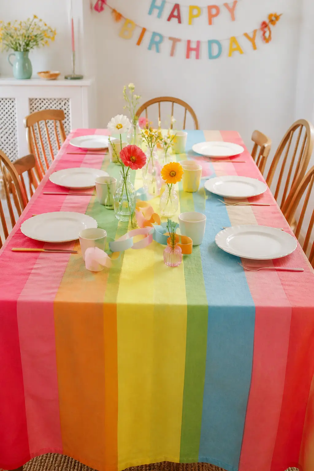Rainbow Stripe Tablecloth Base — Use a wide rainbow stripe tablecloth as the base layer, then set white plates directly on top so the stripes frame each place