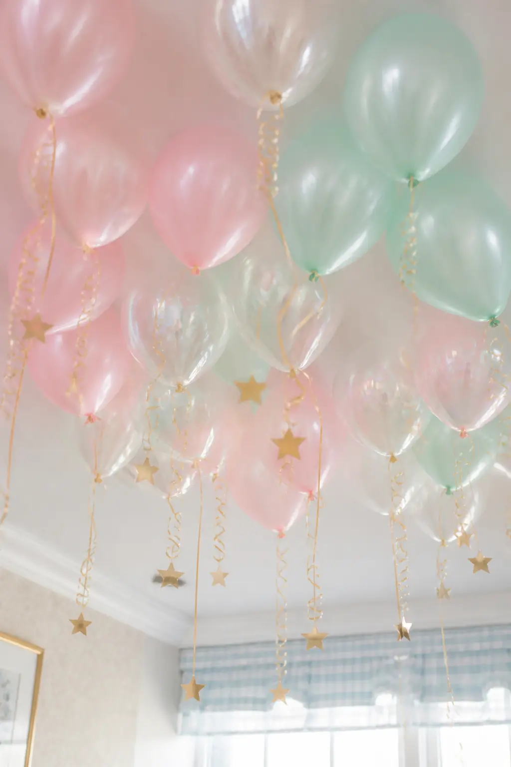 Iridescent Balloon Ceiling Cloud — A cluster of helium balloons, half in pearl-finish pastels and half in clear iridescent, gathered at the ceiling above the