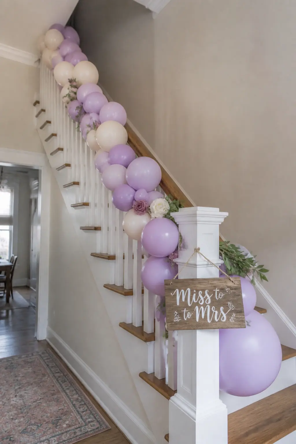 Lilac and Cream Garland Along the Stair Banister with a Hand-Lettered Sign — A lilac and cream balloon garland winds loosely along a stair banister, tied at