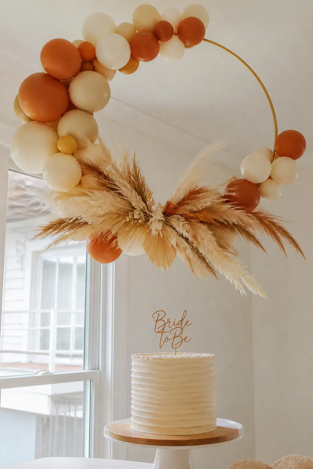 Terracotta and Cream Hoop Above the Cake — A hoop of terracotta and cream balloons hangs from the ceiling directly above the cake table. Bridal shower balloon
