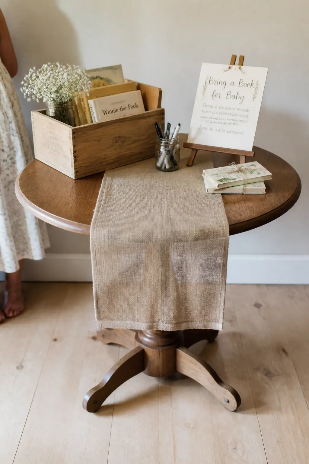 The Linen Runner as Ground Line — A strip of linen or a folded tea towel across the table surface unifies everything sitting on it: crate, sign, pen, candle.