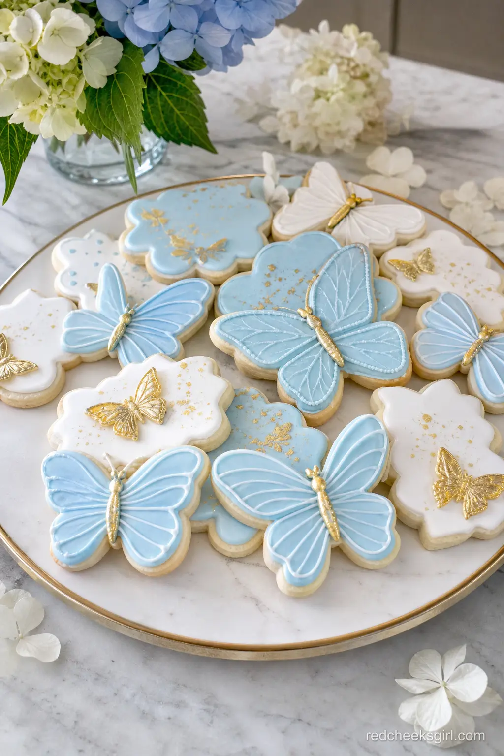 Butterfly Sugar Cookie Platter — A platter of iced sugar cookies in sky blue and white, each piped with a simple gold-dusted butterfly, gives guests something