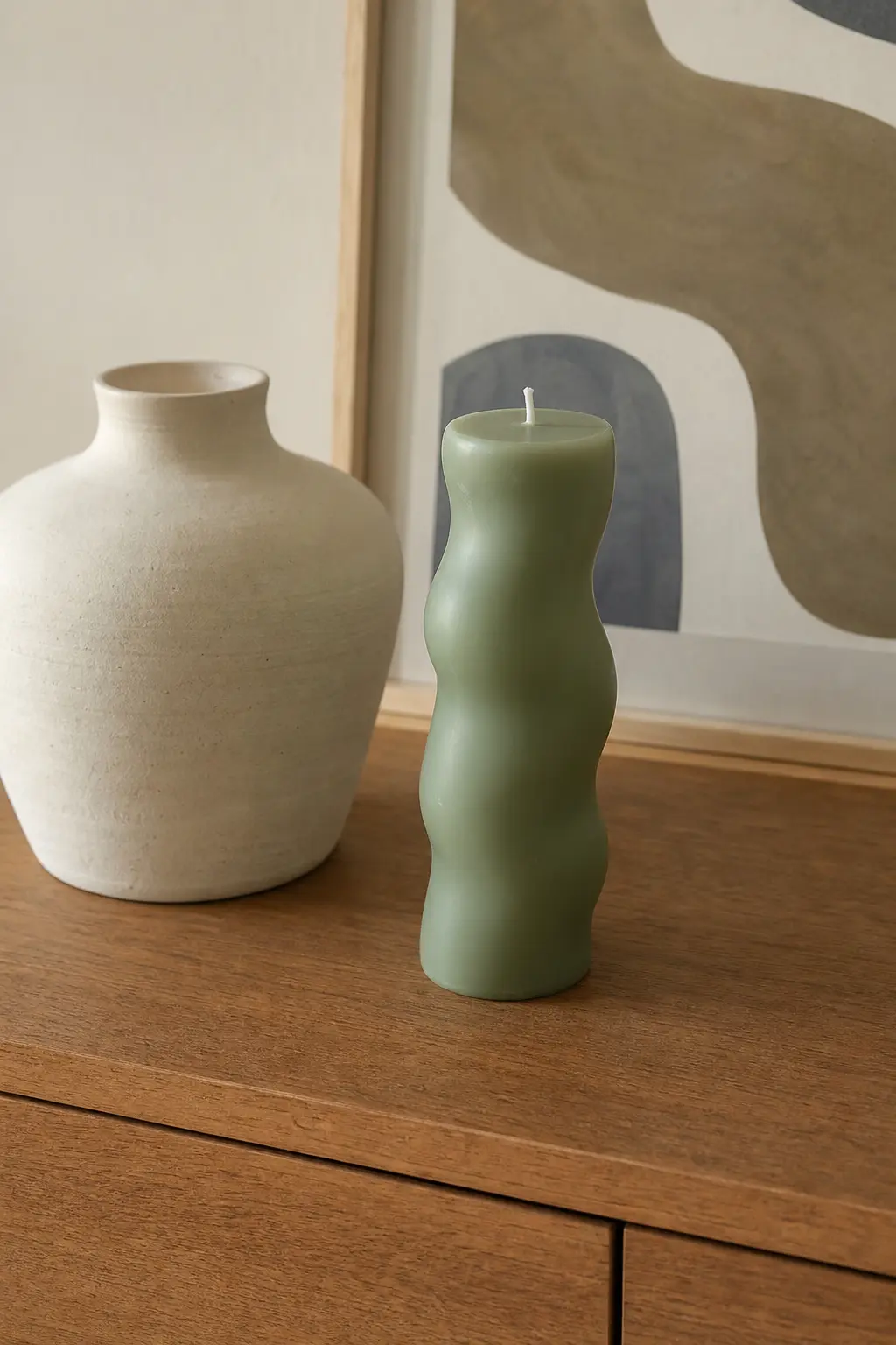Abstract Wave Blob Pillar — An organic, freeform blob pillar in sage green, all soft curves and no straight edges, sits on a console beside a plaster vase and