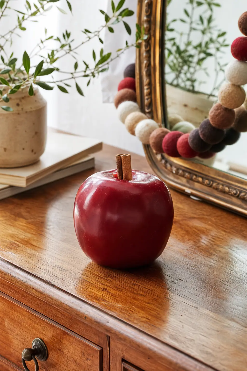 Apple Candle with Cinnamon Stem — A deep red apple candle finished with a real cinnamon stick pushed in as a stem while the top is still soft is a small detail