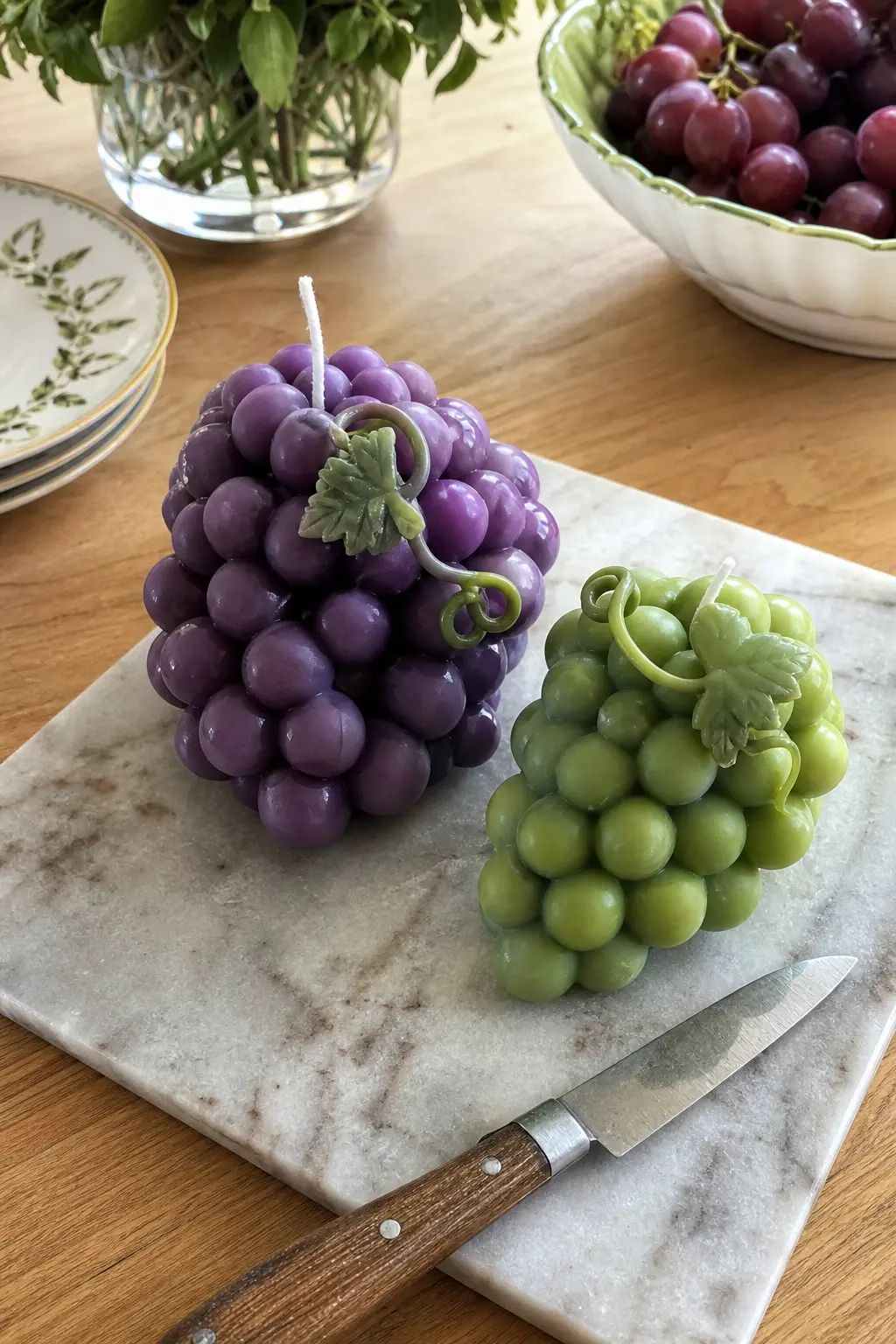 Grape Cluster Candle — A grape cluster candle, purple fading to green at the tips, sits on a marble cheese board looking closer to fruit than to a candle until