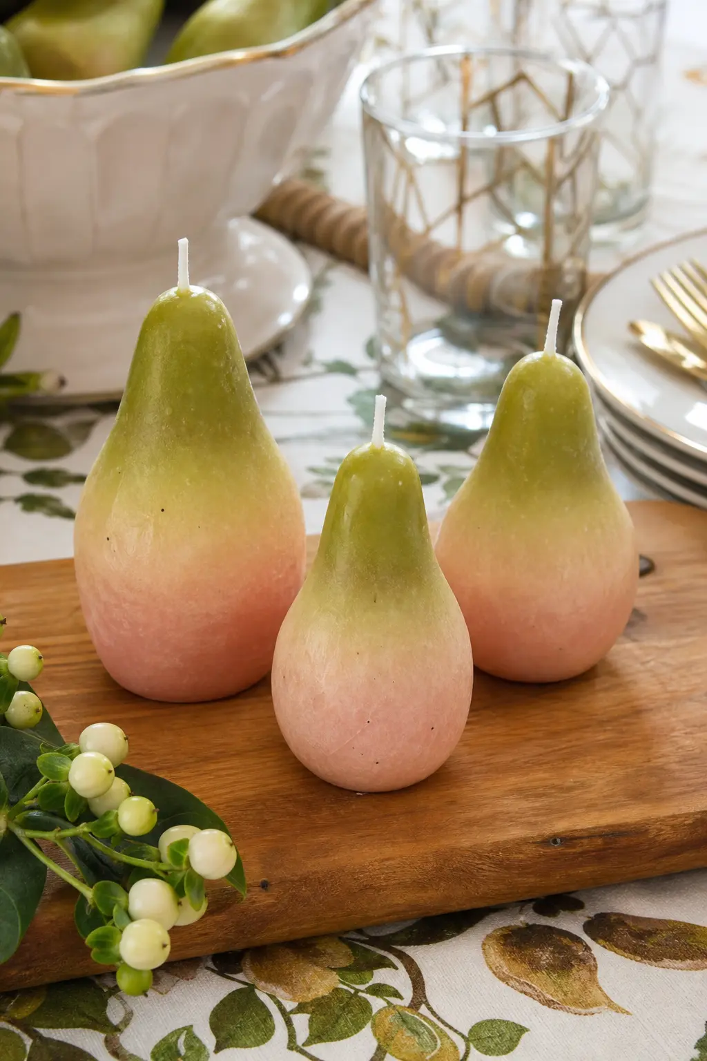 Ombre Pear Trio — Three pear candles dipped from green to blush at the base sit together on a wooden cutting board, their ombre finish doing most of the visual