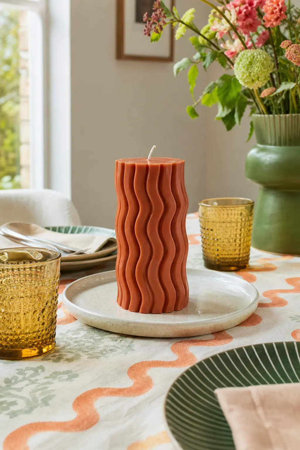 Wavy Ribbon Pillar — A wave-textured pillar in terracotta and rust looks handmade in the good sense, with clove and orange fragrance leaning into an autumnal