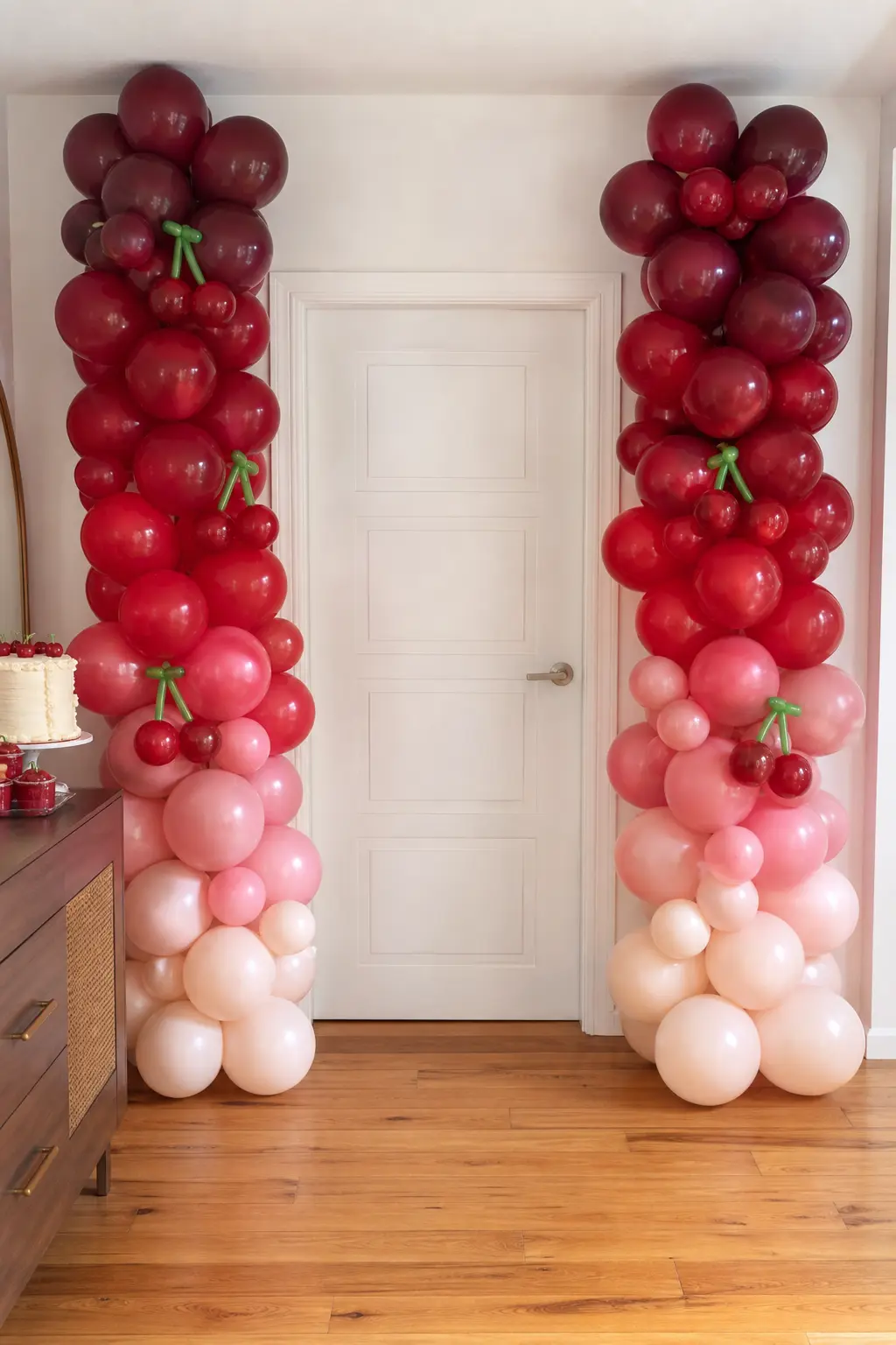 The Blush to Wine Balloon Columns — Two balloon columns flank an entrance or a cake table, each running an ombre from pale blush at the base to deep wine at