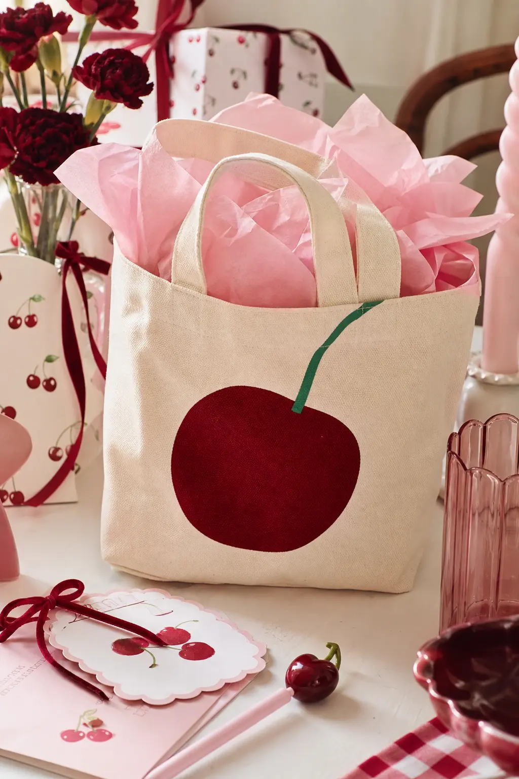 The Cherry Print Treat Tote — A small canvas tote printed with a single oversized cherry graphic in deep red comes filled with pink tissue paper and a few