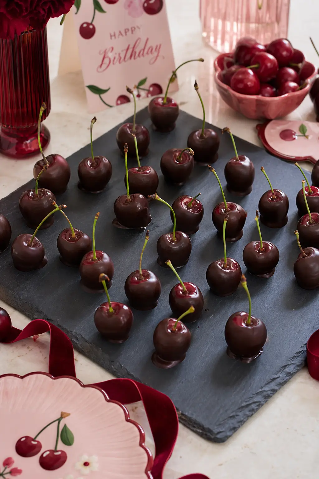 The Dark Chocolate Cherry Board — Rows of dark chocolate dipped cherries with their stems left on cover a slate board, arranged by size rather than in perfect