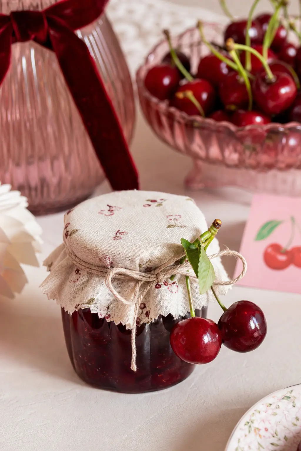The Mini Cherry Preserve Jar — A tiny glass jar of cherry preserves gets a scrap of gingham-free cream fabric over the lid, tied with plain twine and a single