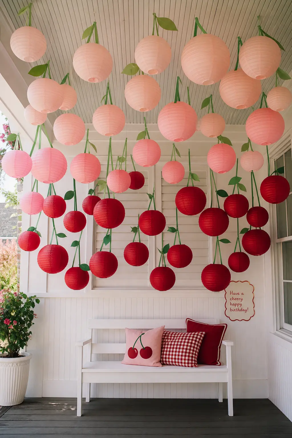 The Ombre Cherry Lantern Canopy — Round paper lanterns shaped and painted like cherries hang in an ombre run from pale blush at the edges to deep red at the