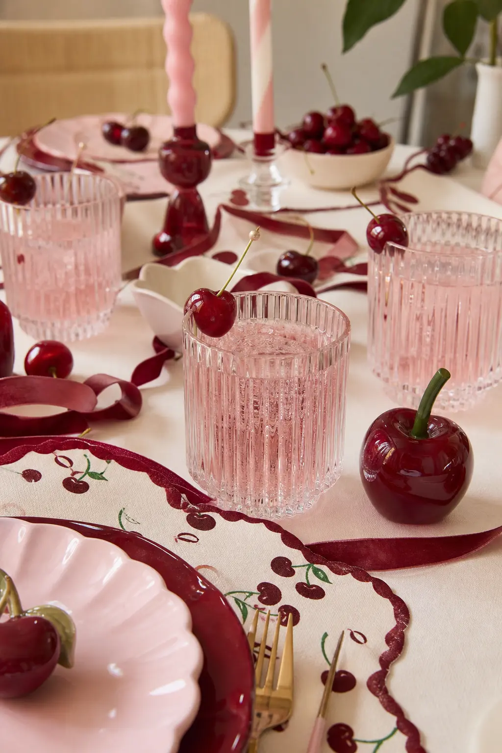 The Ribbed Glass and Cherry Stirrer Setting — Ribbed clear glass tumblers hold a pale pink drink at each place, each finished with a fresh cherry threaded onto