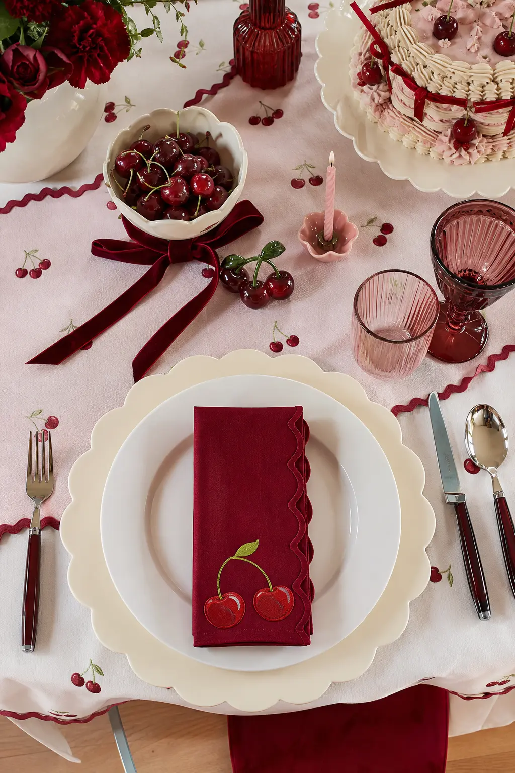 The Scalloped Cream Place Setting — Scalloped edge charger plates in soft cream sit under simple white dinner plates, with a folded cherry red cloth napkin as