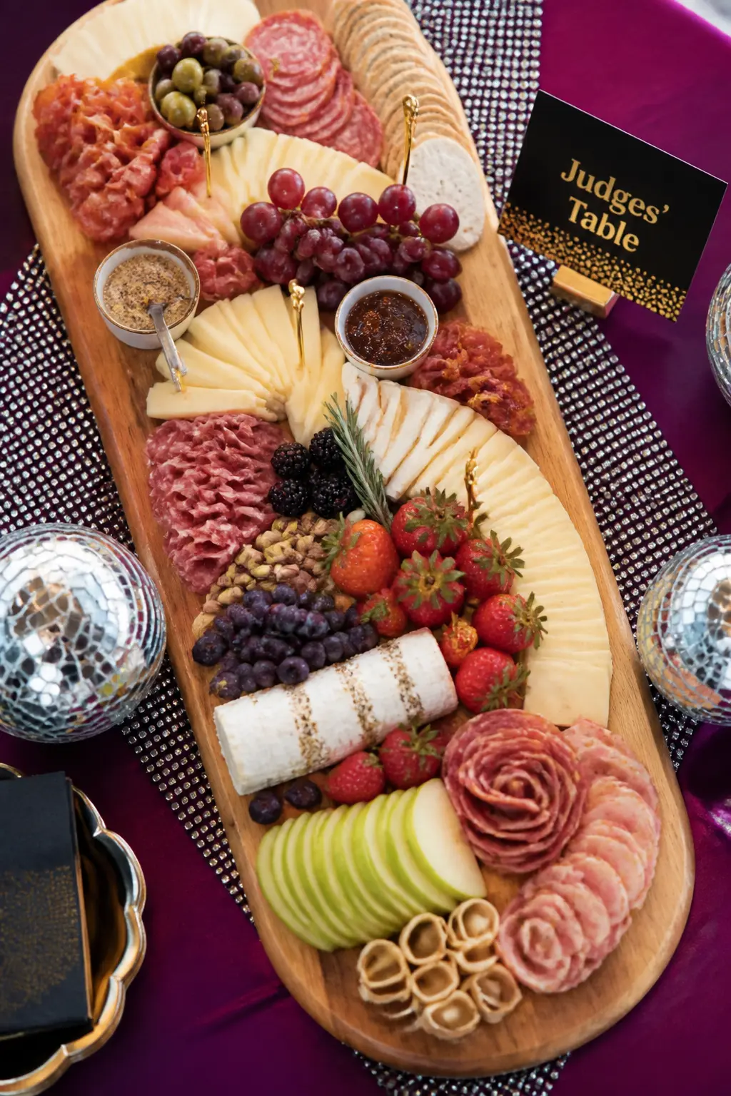 "Judges' Table" Charcuterie Board — A large charcuterie board is labelled at one end with a small standing card that reads "Judges' Table." The food is