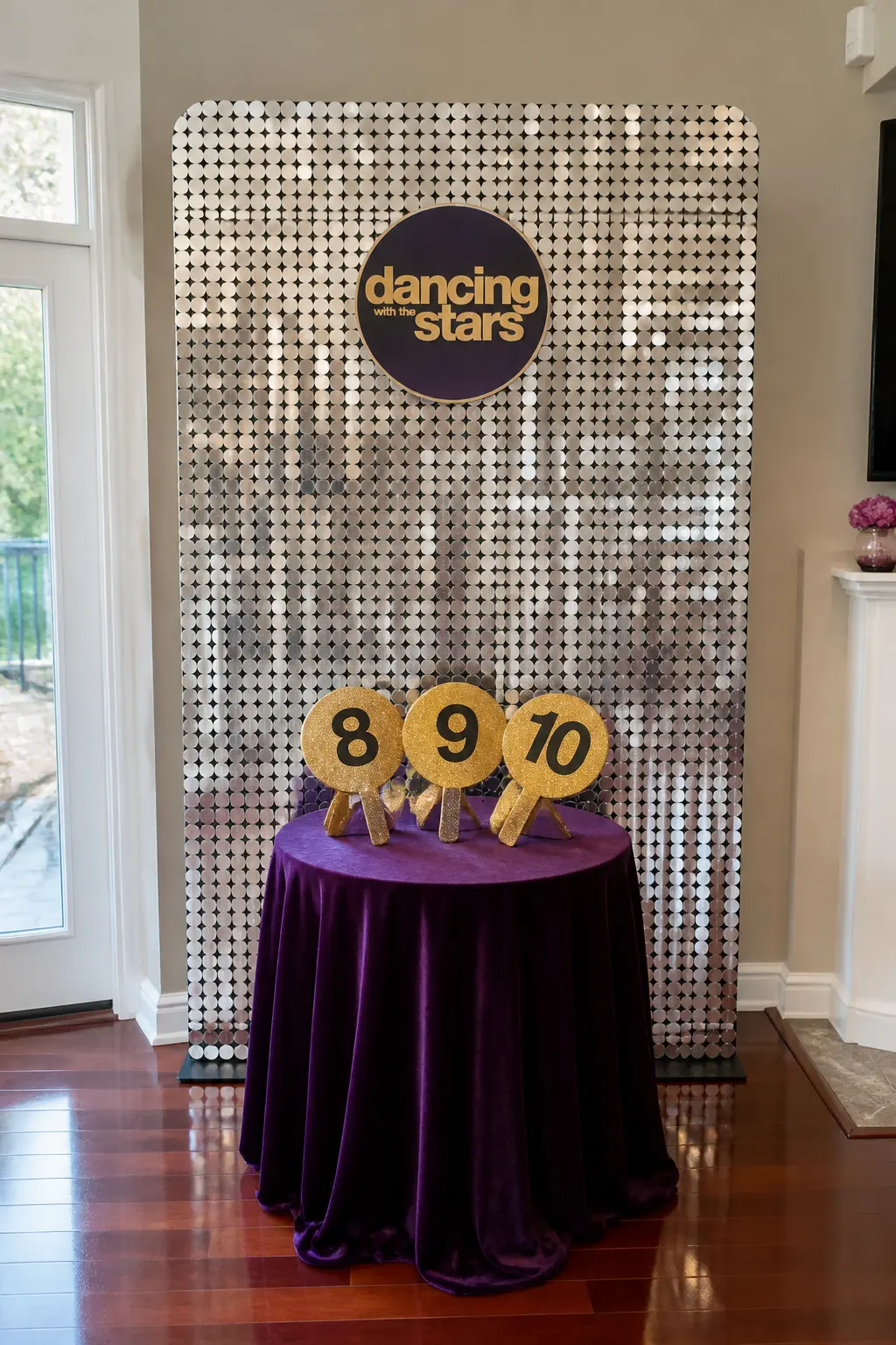 Scoring Paddle Photo Backdrop Station — A wide sequined backdrop panel in silver or gold, hung against a wall, has a small table in front of it holding three