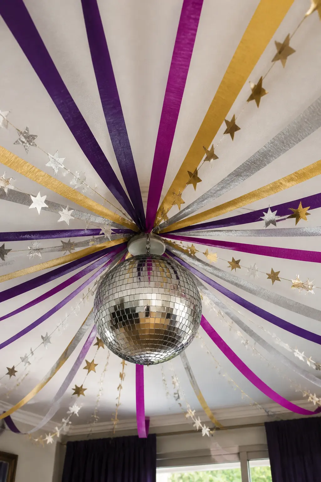 Streamer and Disco Ball Ceiling — Wide crepe streamers in violet, gold and soft silver fan out from a central point on the ceiling to the four corners of the