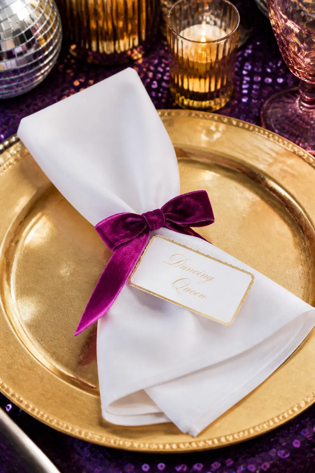 Velvet Ribbon Place Settings With Calligraphy Name Tags — A short length of violet velvet ribbon tied around each folded napkin, with a small gold-edged card
