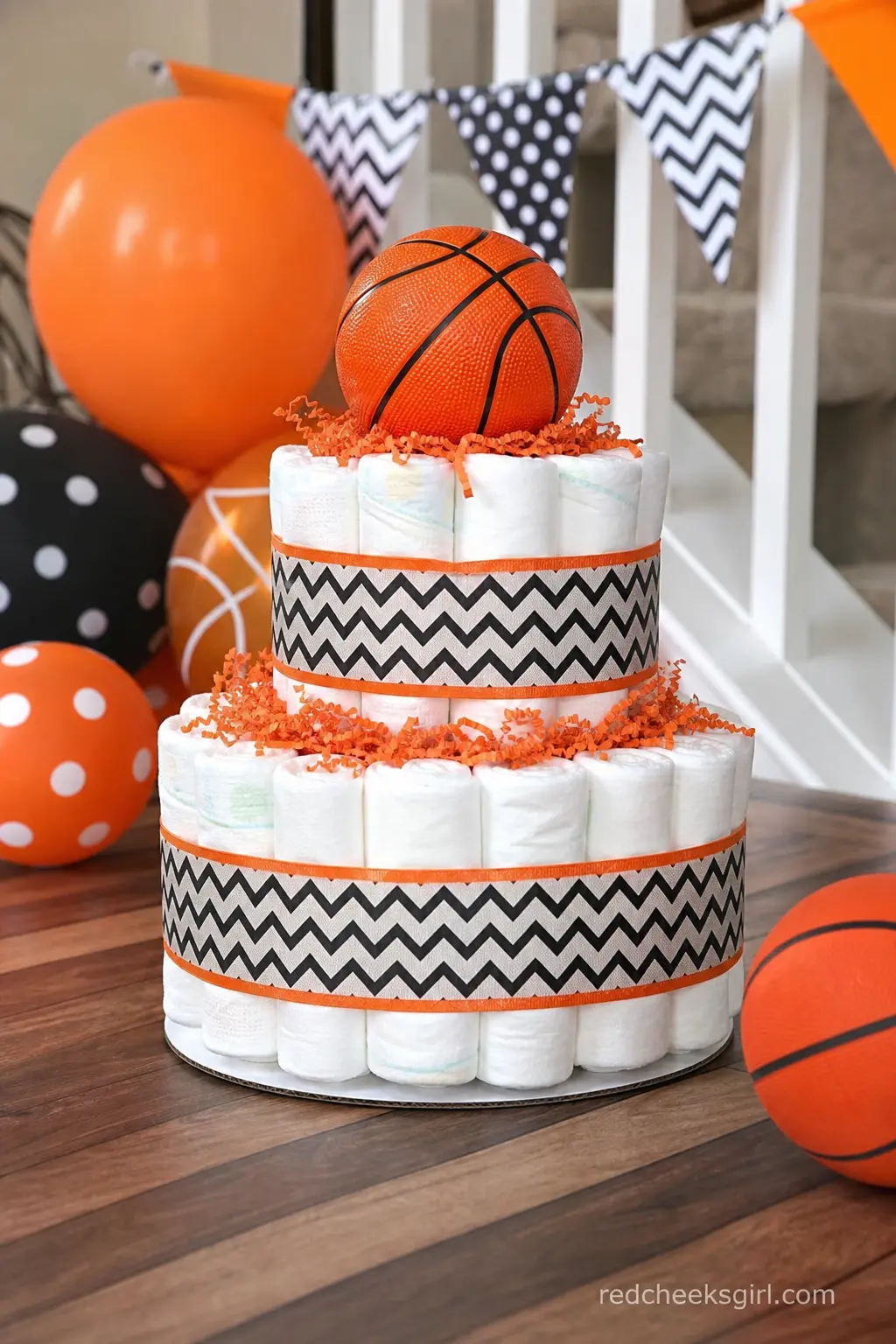 Basketball Diaper Cake — Orange and black ribbon in a herringbone pattern wraps the tiers, and a small orange and black basketball sits balanced on top. Diaper