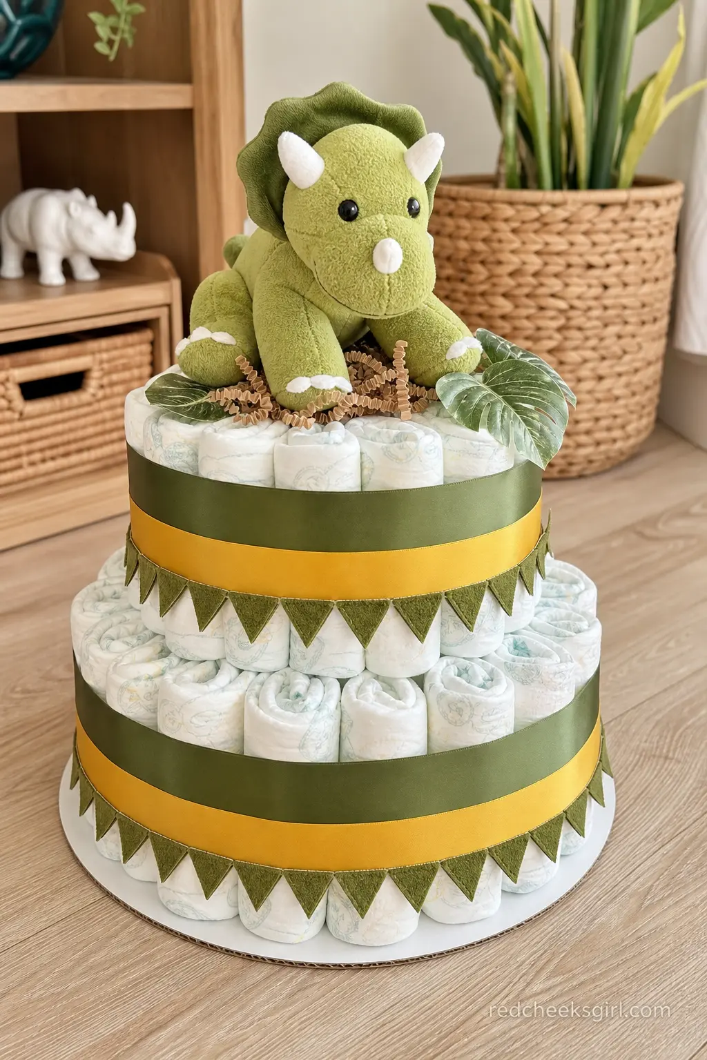 Dinosaur Diaper Cake — Olive green ribbon with a mustard yellow band wraps the tiers, finished with a triangle scale trim that mimics dinosaur skin, and a soft