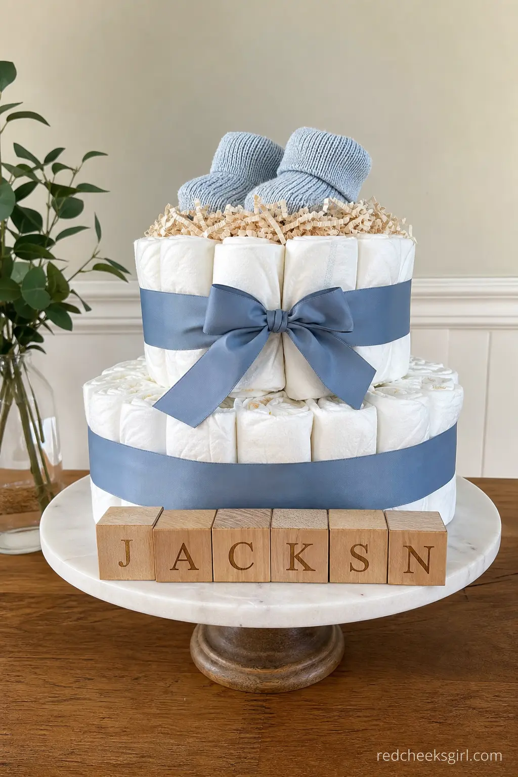 Personalized Name Diaper Cake — Dusty blue ribbon wraps the tiers, and small wooden blocks spelling the baby's name line up along the base instead of a single