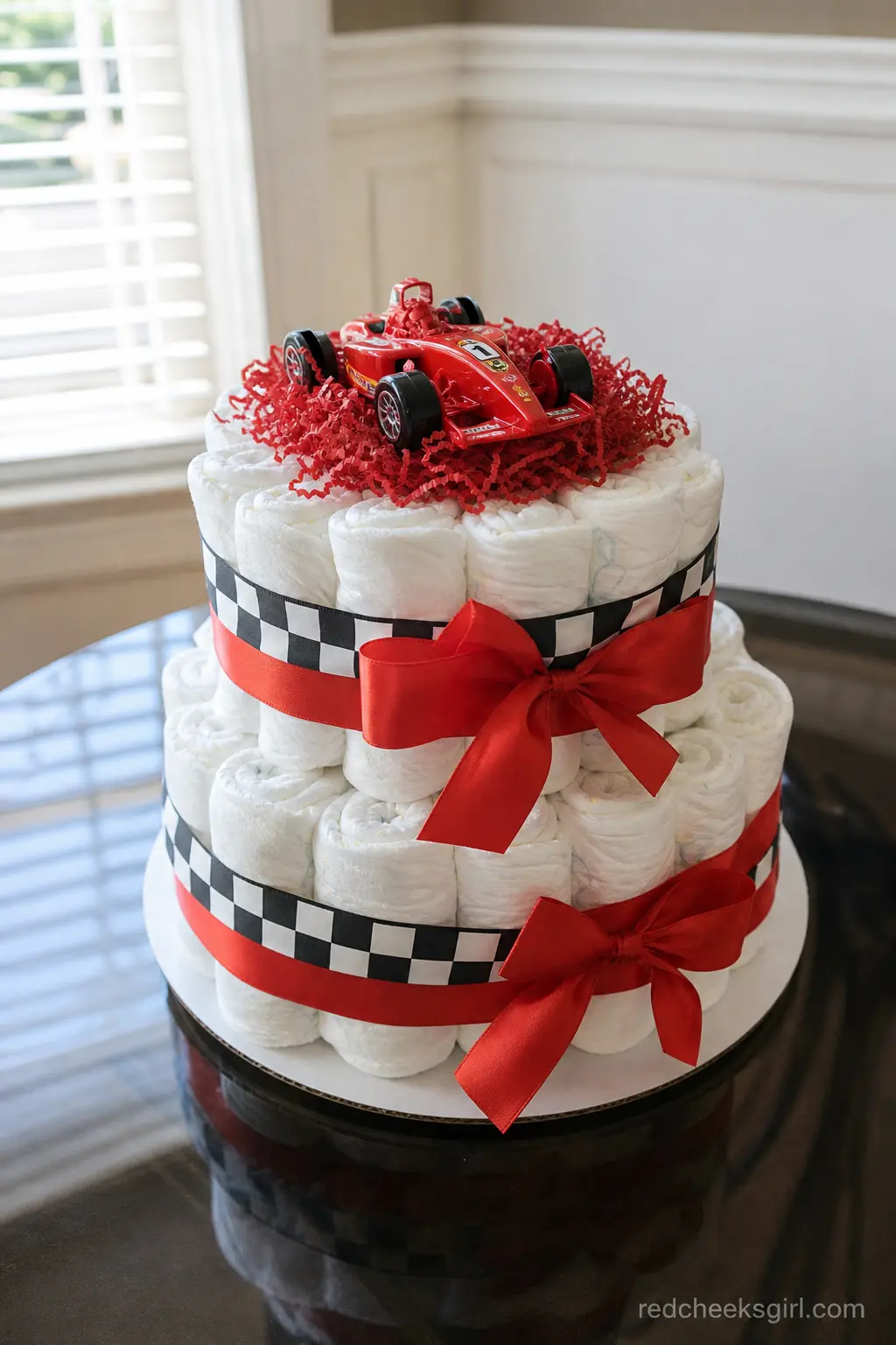 Race Car Diaper Cake — A checkered flag band wraps the middle tier, red ribbon finishes the top and bottom, and a small die cast race car sits at the very top