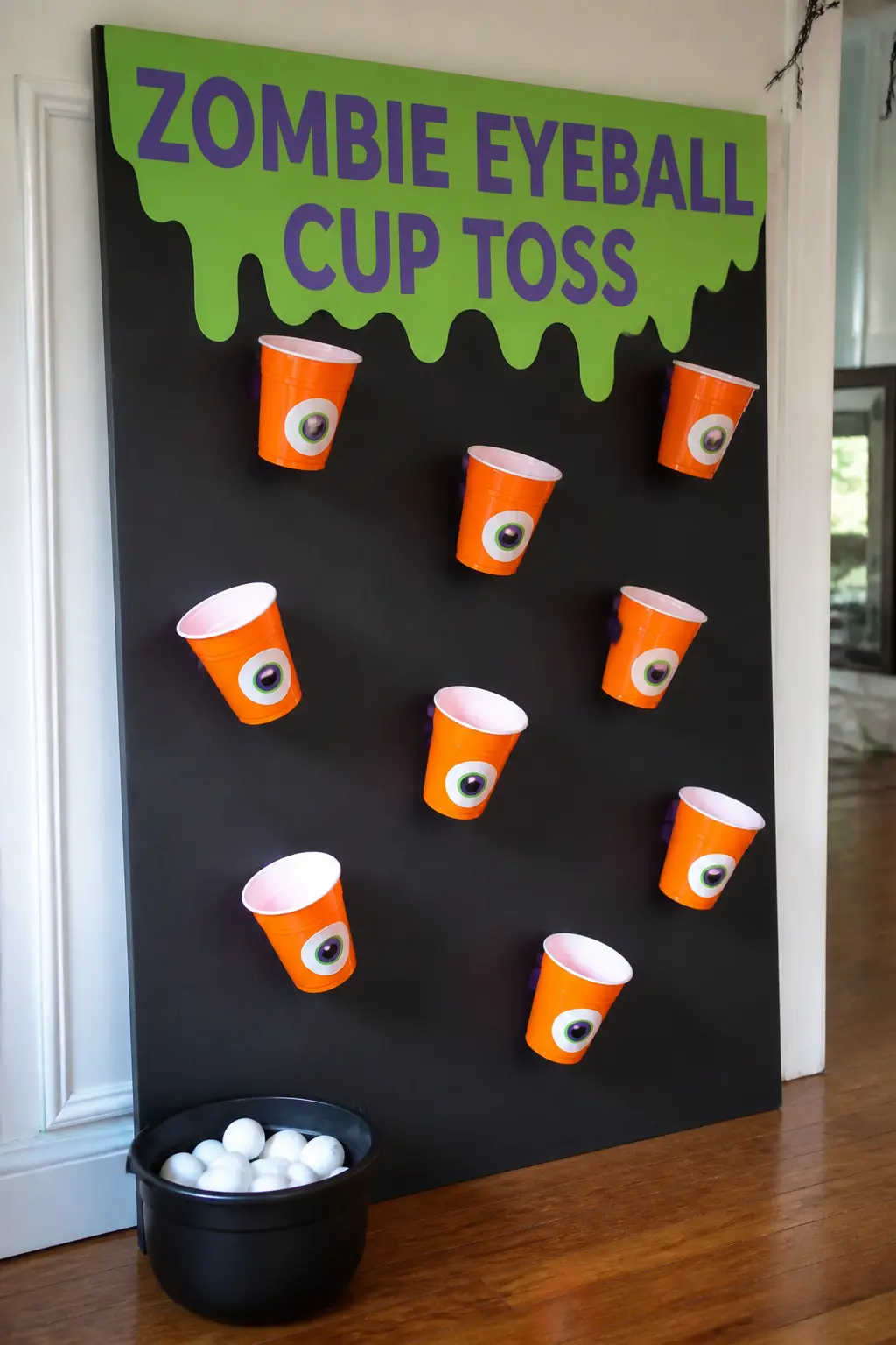 Zombie Eyeball Cup Toss — Paint a large sheet of black foam board and stick orange plastic cups to it with hot glue, open end facing forward, in a staggered