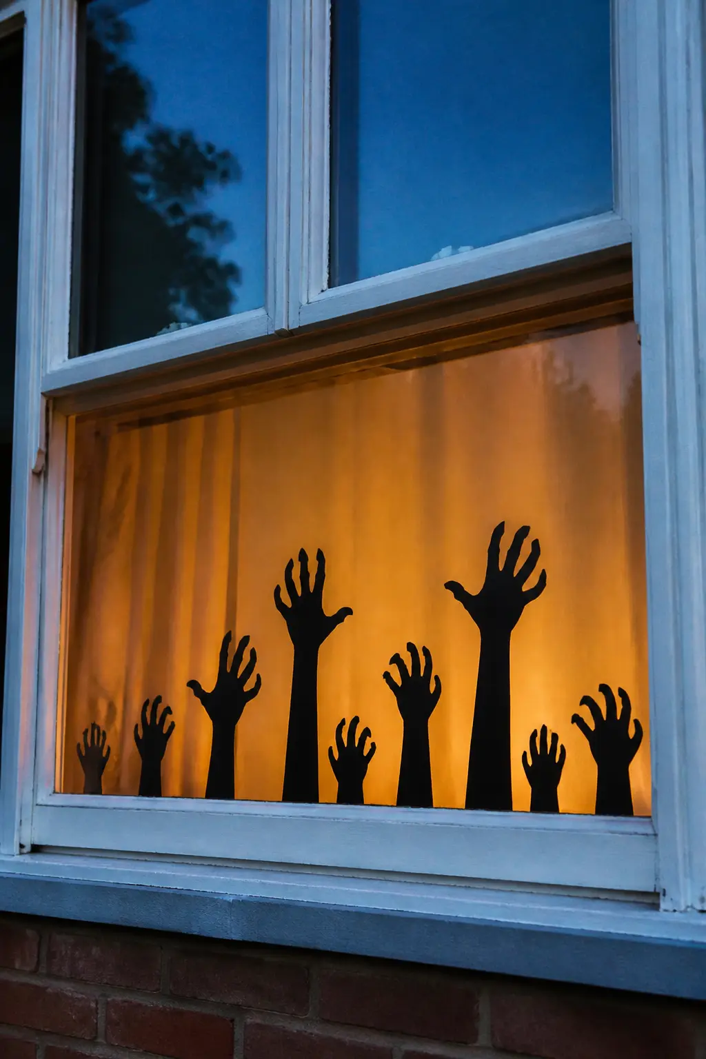 Zombie Hands at the Sill — Cut ten to twelve hand-and-arm shapes in varying lengths and poses from black cardstock, all reaching upward. Diy halloween window