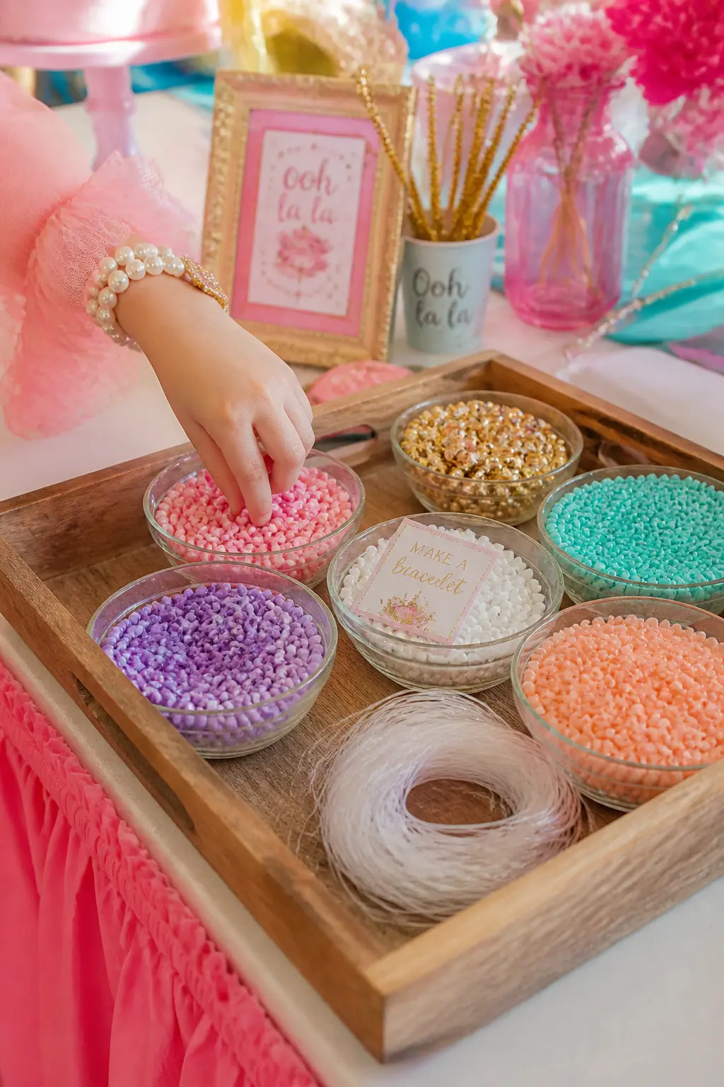 Bead Bracelet Making Station — Lay a flat tray of sorted beads in pink, gold, aqua and purple at child height, with pre-cut elastic already threaded with a