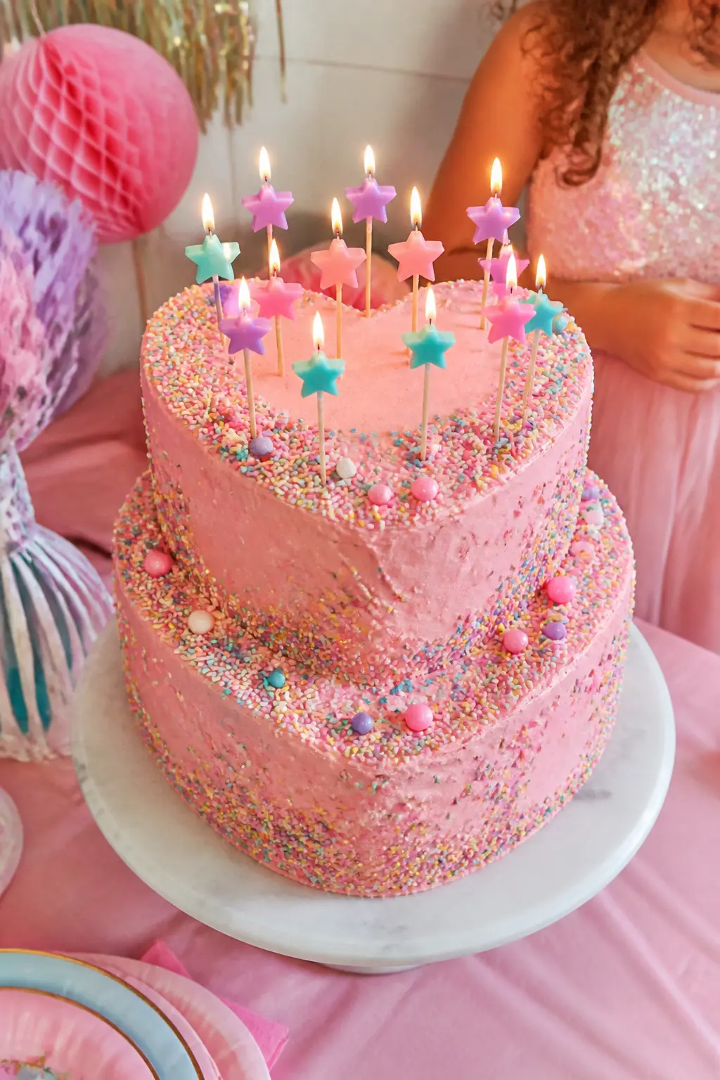 Heart-Shaped Pink Sprinkle Cake — A heart-shaped cake in pink buttercream, finished with a star-tip border and saturated with rainbow sprinkles, is the single