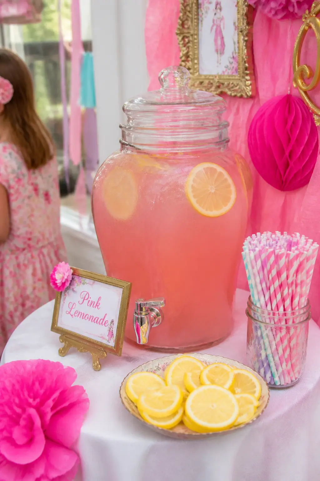 Pink Lemonade Drinks Station — Set a glass beverage dispenser filled with pink lemonade on a small side table alongside a bucket of ice, a jar of paper straws