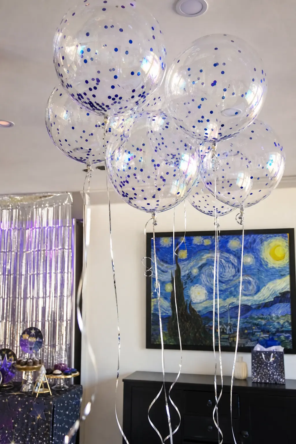 Iridescent Bubble Cloud — A loose cluster of clear iridescent bubble balloons, each holding a scatter of small cobalt confetti inside, floats near the ceiling