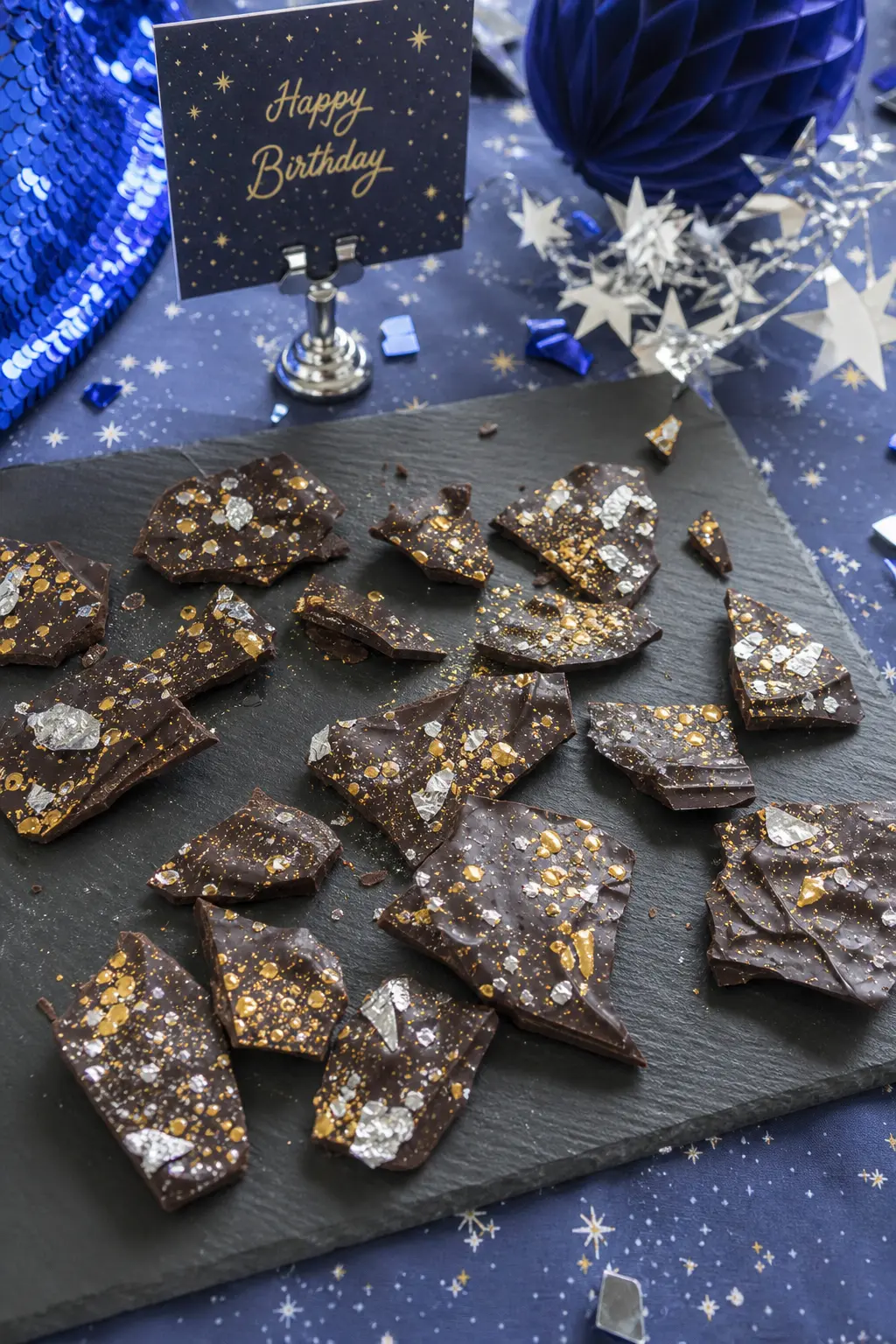 Meteorite Chocolate Bark — Dark chocolate bark, snapped into rough shards and dusted with edible silver leaf and a little gold dust, sits on a plain black