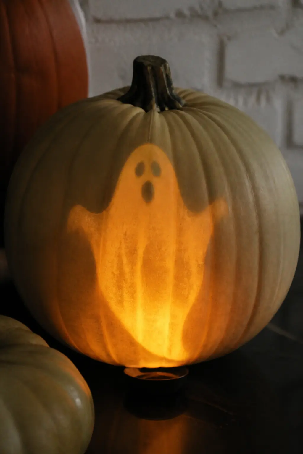 Ghost Only Visible When Lit From Below — The ghost is painted in a color that matches the pumpkin in daylight but catches a warm light source directed upward