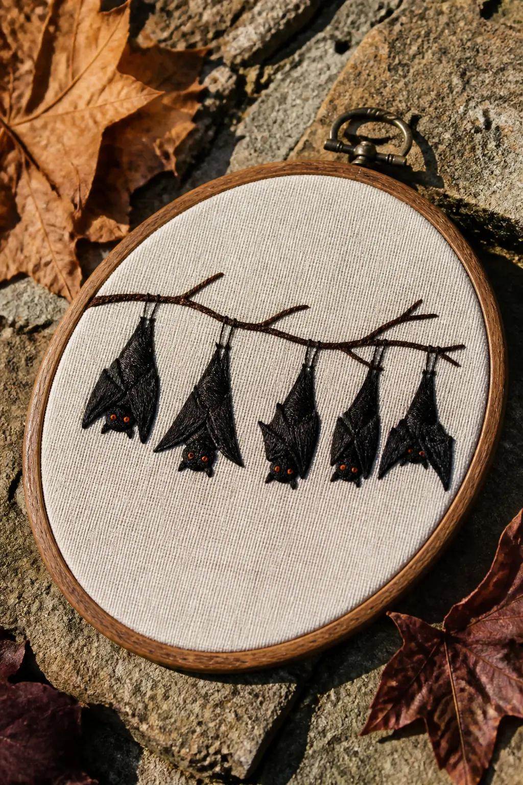 Bat Colony on Branch — A bare horizontal branch in dark brown stem stitch, with five bats hanging upside down from it in various states of wing-fold, rendered