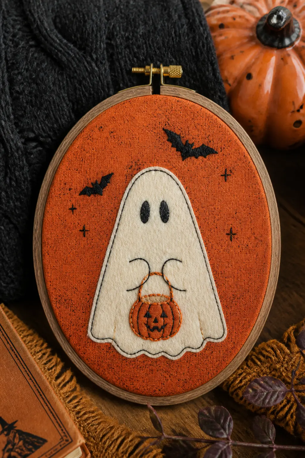 Ghost with a Pumpkin Bucket — The ghost body is a piece of cream felt cut to a soft rounded shape and whip-stitched onto an orange patterned fabric background.