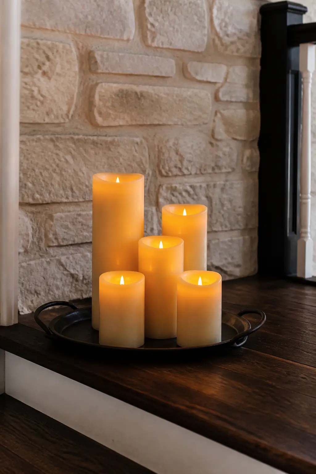 Pillar Candle Cluster on the Landing — Group five to seven pillar candles of varying heights on a low metal tray or a thick wooden board on the stair landing.