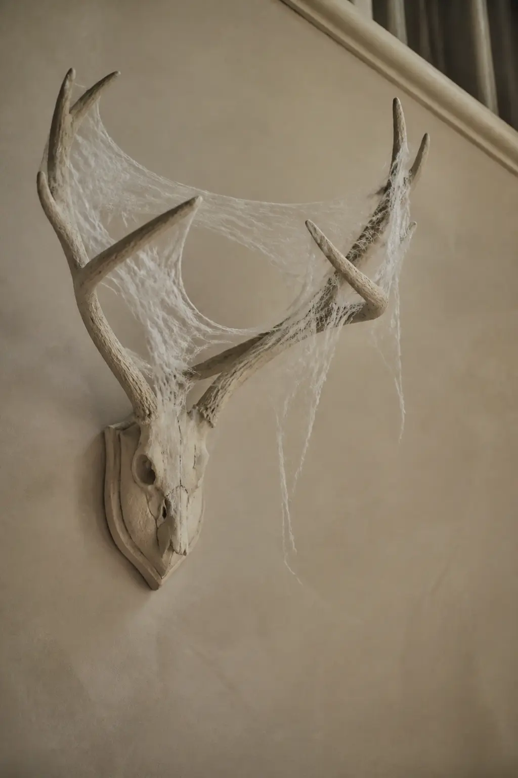 Wall-Mounted Antler with Cobweb Stretch — Mount a resin or natural antler set on the staircase wall and stretch fine white cobweb cotton between the tines.