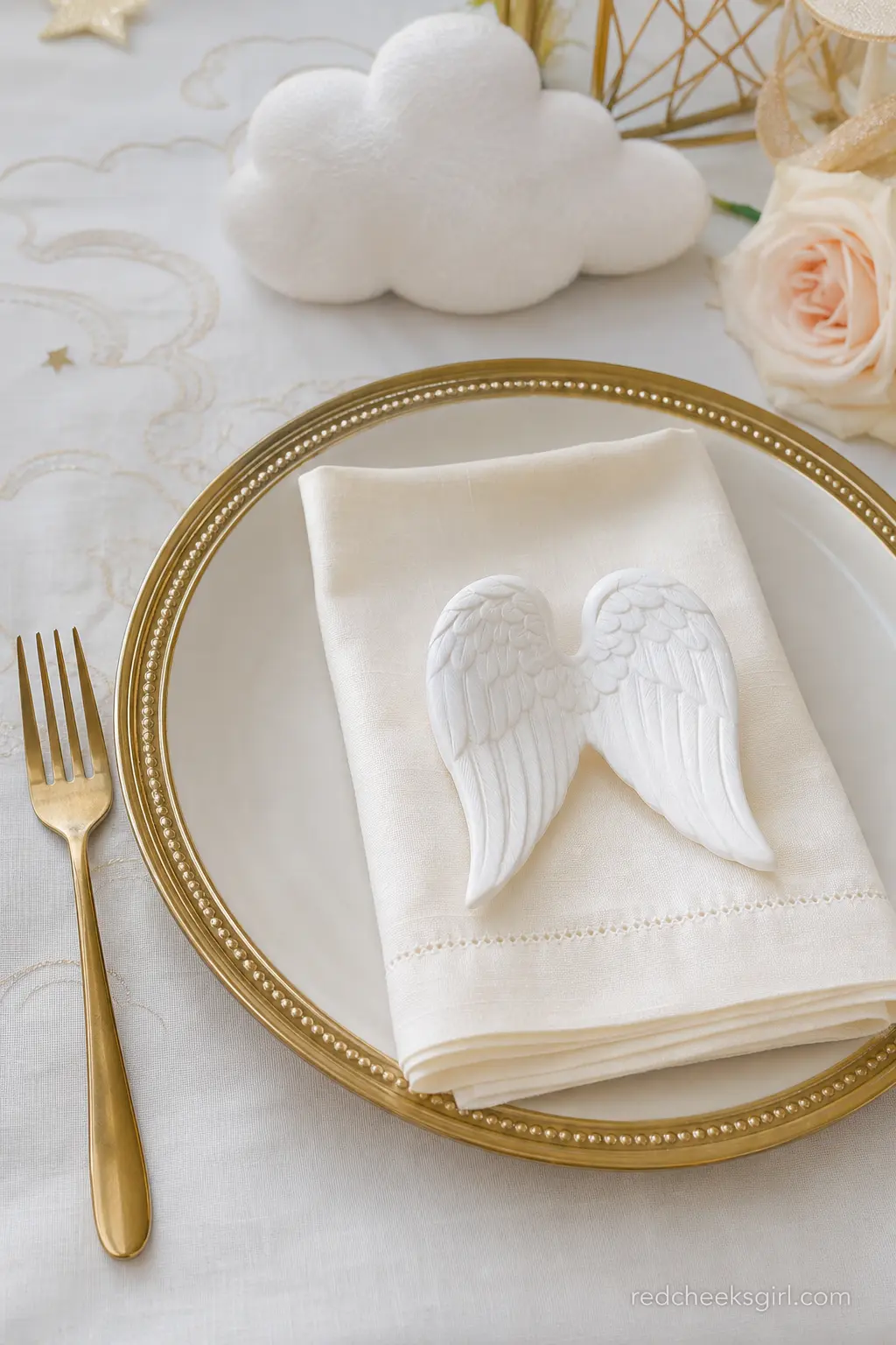 An Angel Wing Place Setting — A gold rimmed charger plate, a folded ivory napkin and a single small angel wing ornament laid across the top turn an ordinary