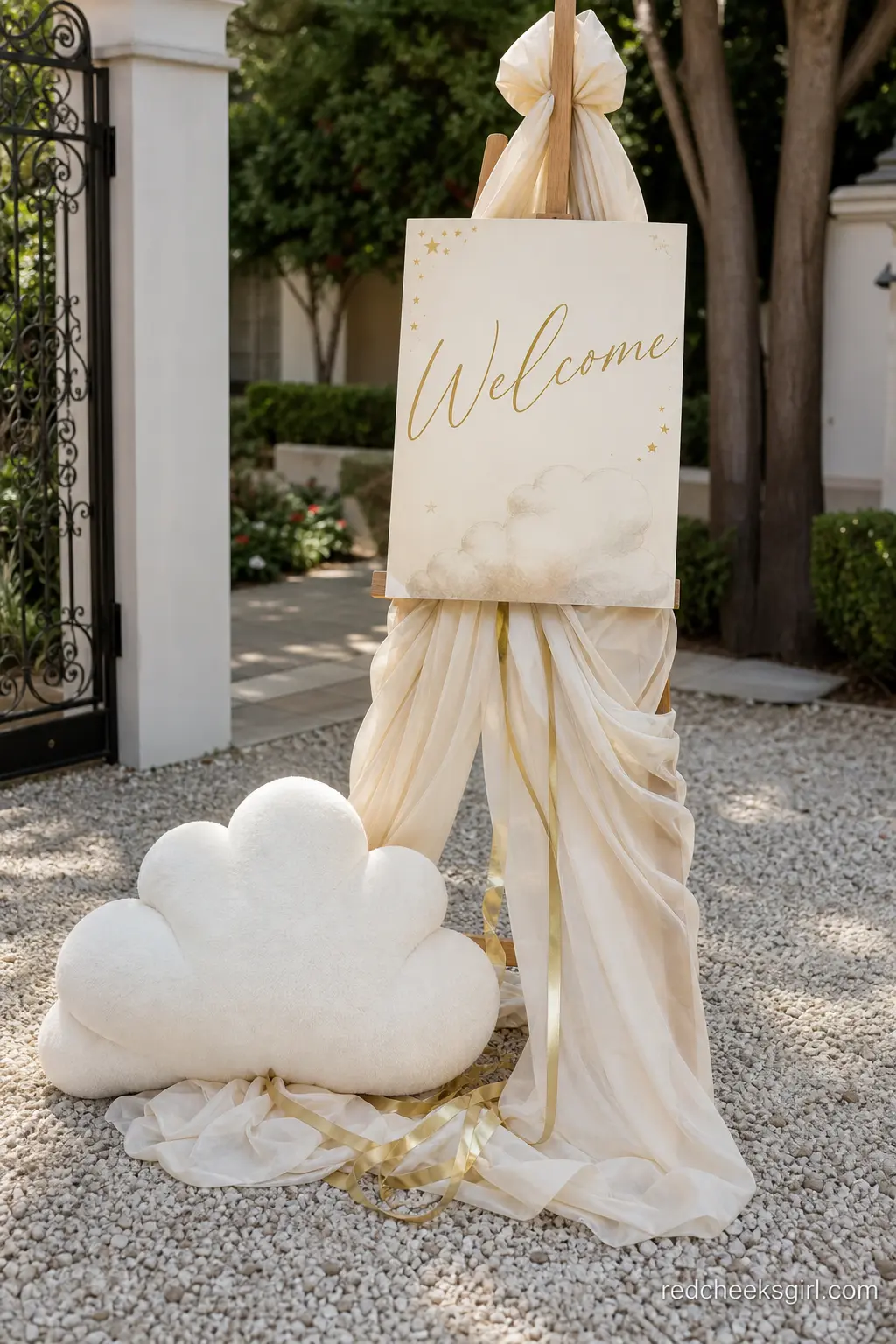 A Draped Welcome Sign With a Cloud at Its Base — A plain wooden easel, wrapped in ivory fabric and tied off with a wide silk ribbon, does more work than any