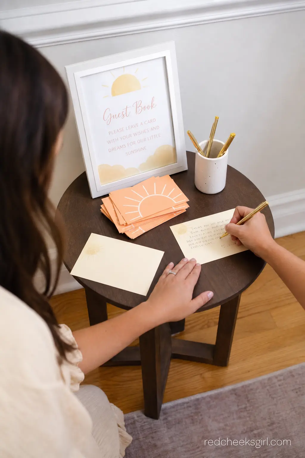 Guest Book Station With Sun Cards — A small side table holding a stack of peach and cream cards where guests write a note instead of signing a book gives every