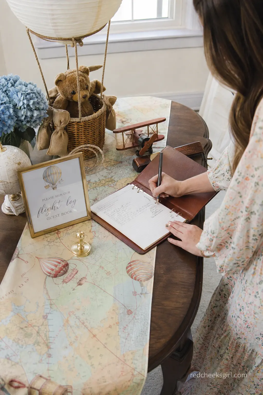 Flight Log Guest Book Station — A guest book styled as a flight log, brown leather on a vintage map runner with a small gold ink stamp beside it, gives guests